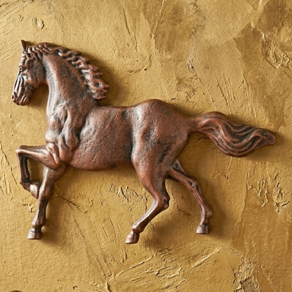 Bronze horse sculpture on a textured gold wall with a wooden shelf below featuring a compass and spurs.